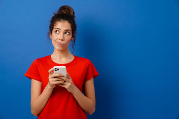 Young brunette woman grimacing while using mobile phone