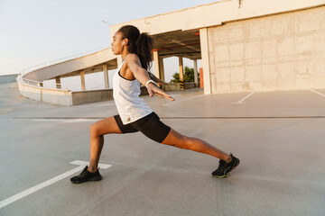 Fototapeta premium Black sportswoman listening music while working out at parking outdoors
