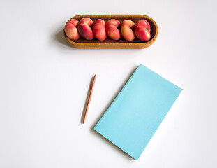 Creative office style table, blue notepad cover, rose-gold pen and ripe flat donut peaches in cork...