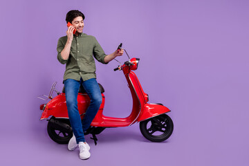 Fototapeta na wymiar Full size photo of happy young positive man hold hand phone rider bike talk phone isolated on violet color background