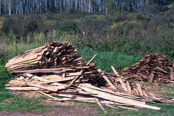 Lumber stockpiled in the open air on the green grass.