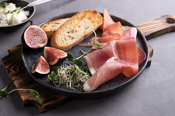 Italian antipasto from prosciutto, toast, cream cheese on a cutting board on a gray background, ham...