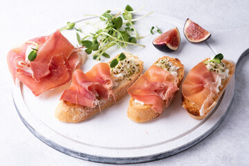 Crostini with prosciutto on a white background, antipasto of ham, ricotta and microgreens.