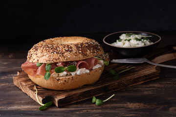 Prosciutto and cheese sandwich, cutting board with ham and ricotta bagels on a dark wooden...