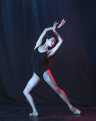 Young and graceful female ballet dancer in motion isolated on dark background in neon light. Art, motion, action, flexibility, inspiration concept.