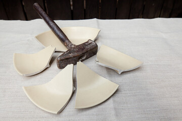 Broken plate and a metal hammer lying on a tablecloth.