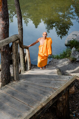 high angle view of buddhist in orange robe walking on wooden stairs near lake