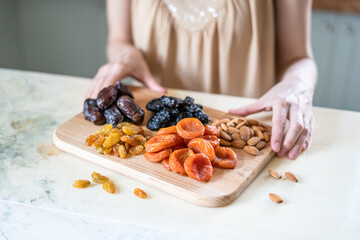preparing a healthy breakfast, dried apricots, raisin, prunes, dates and almonds on a wooden cutting board in the kitchen on the table. Dried fruit in female hands