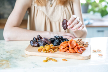 preparing a healthy breakfast, dried apricots, raisin, prunes, dates and almonds on a wooden cutting board in the kitchen on the table. Dried fruit in female hands