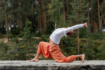 side view of buddhist in sweatshirt and harem pants practicing crescent lunge pose outdoors