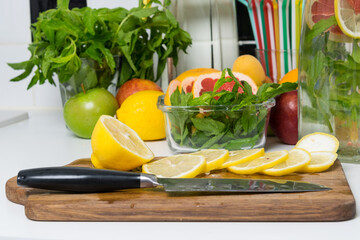 on a wooden board, a juicy yellow lemon is cut into slices with a sharp knife, for making a refreshing drink with mint
