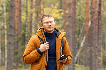 Portrait of a Caucasian man with a smartphone in his hand. A man catching a cellular network on a smartphone while walking in the forest © lizaelesina