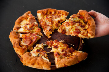 Close of hand holding cheese pizza with wooden board and black background