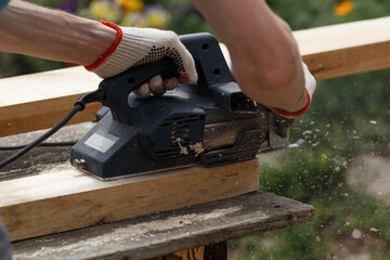 A carpenter planks wood with an electric plane. Woodworking carpentry. Close-up. Man in the garden...