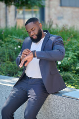 A dark-skinned man in a suit looking at the watch