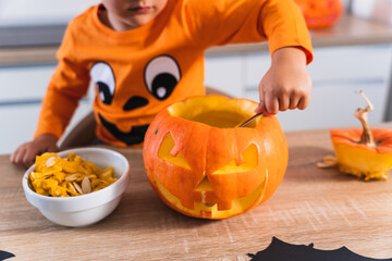 Close up of a child dressed in a halloween pumpkin t-shirt opening and emptying a halloween pumpkin and decorating it for the halloween party.