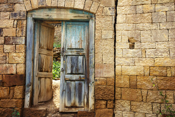 antique door with old blue paint, shabby from time to time. Stone wall with a doorway and a door in...