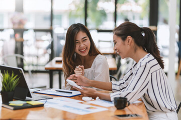 Two young Asian businesswoman are happy working together brainstorm ideas for success using calculator document graph at the office.