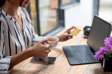 Image of a businesswoman sitting and drinking coffee holding a credit card online shopping using tablet and smartphones placed at the table.