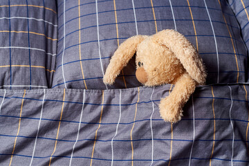 Stuffed rabbit in bed with pillows and duvet.