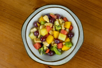 refreshing fruit salad , natural colors served in crockery container and small white plate , white wooden background in photo taken from above with space for text on the side