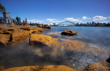 Sydney Harbour with nice rocks in the foreground the soft waves crashing on the shore and the...