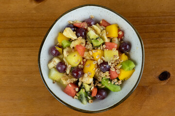 fruit salad with natural cereals served on white tableware , wooden background in photo taken from above with space for text on the side
