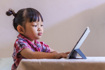 Portrait image of 3-4 years old preschool kid. Bored Asian child girl using and touching smart pad or tablet for do her homework and online learning (E-learning). Back to school, Study from home.