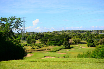 View of Golf Course with putting green, green grass, sand bunker, blue sky, and high voltage electric transmission tower background. Using for Golf field banner with a copy for your text.