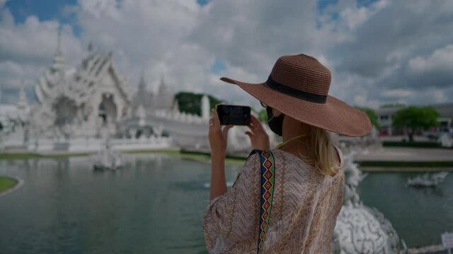 Chiang Rai, Thailand - 17 July 2020: Woman tourist making picture of Wat Rong Khun, known as the White Temple. Handheld shot