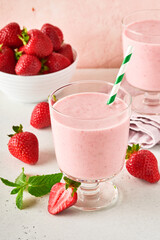 Two strawberry smoothie or milkshake with berries and mint in glass on light pink background. Summer drink shake, milkshake and refreshment organic concept. Healthy dieting, vegetarian food concept.