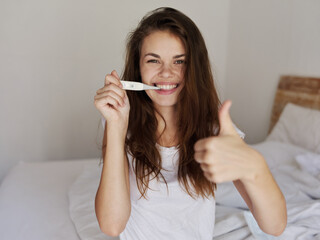 cheerful woman sitting in bed with a thermometer in her hands a positive test