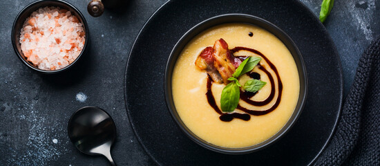 Potato soup cream with bacon and soy sauce in black bowl, on dark old concrete background. Top view