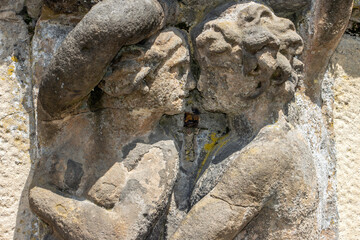 Two stone figures are kissing. Embracing male and female half figures carrying a ledge in a baroque garden