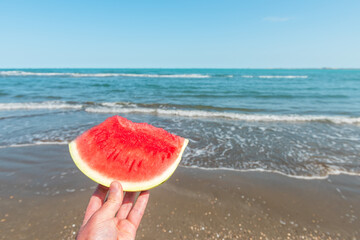 Slice of watermelon in hand on a summer beach