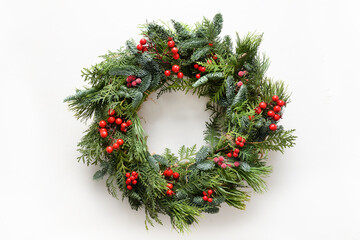 Festive Christmas wreath of fresh natural spruce branches with red holly berries isolated on white background. New Year. Top view. Traditional decoration for Xmas holiday. - obrazy, fototapety, plakaty
