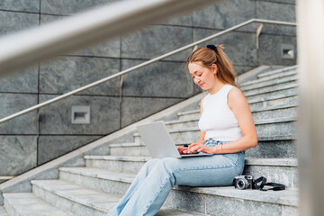 Young caucasian woman flexible worker remote working outdoor sitting staircase using computer