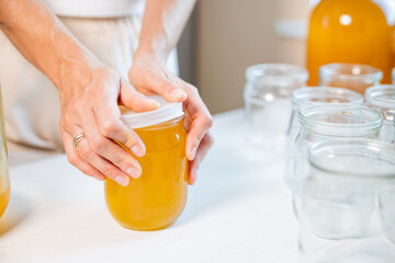 Woman's hands close the lid of a jar of honey standing on a white table and next to a saucer with a spoon