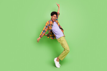 Photo of charming sweet dark skin man wear plaid shirt smiling dancing showing v-signs isolated green color background