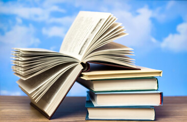 A stack of books on a wooden table. Open book on the background of the sky.