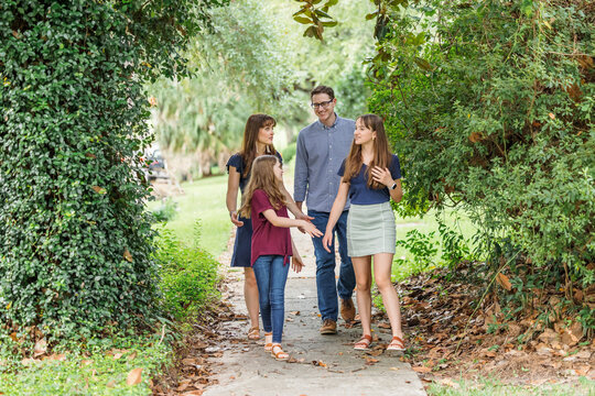A family of a mother and father and two daughters taking a walk in the neighborhood on the sidewalk outside in the summer