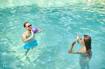 A man and a womna playing ball in a swimming pool