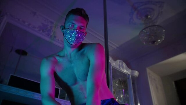 Young shirtless man stripper dancing on camera in mask covered with rhinestones - neon lighting