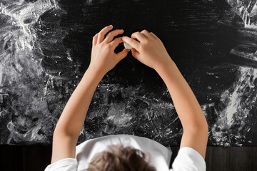 Children's hands knead the dough against a black wooden background with streaks of scattered flour. The concept of Cooking Classes, baking, pizza. Top view.
