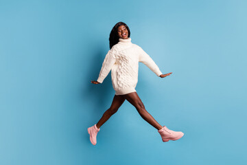 Full length photo of shiny dark skin lady wear white winter outfit walking jumping isolated blue color background