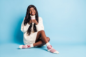 Photo of adorable dark skin lady wear white winter outfit sitting floor coffee looking empty space isolated blue color background