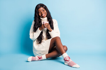 Photo of dreamy cute dark skin woman dressed white winter clothes sitting floor drinking tea isolated blue color background