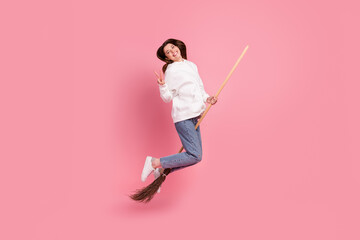 Full body profile photo of young lady jump on broom wear hoodie jeans sneakers isolated on pink background