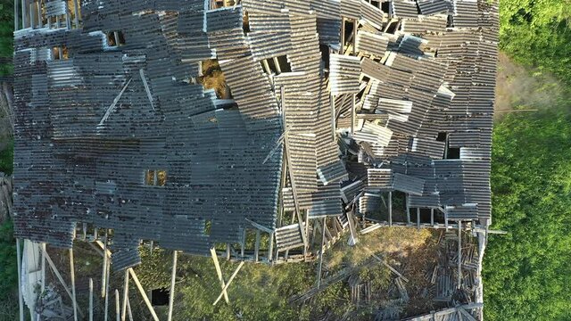 Koeru.Estonia-July 5.2021: Aerial shot of a destroyed rooftop of a soviet farm building. Old structure being taken over by nature. Drone slowly moving backwards with the camera pointed downwards.