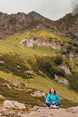 Fototapeta premium meditating young woman in blue sitting on stone in green mountain valley, relaxation in nature, consciousness, mindfulness